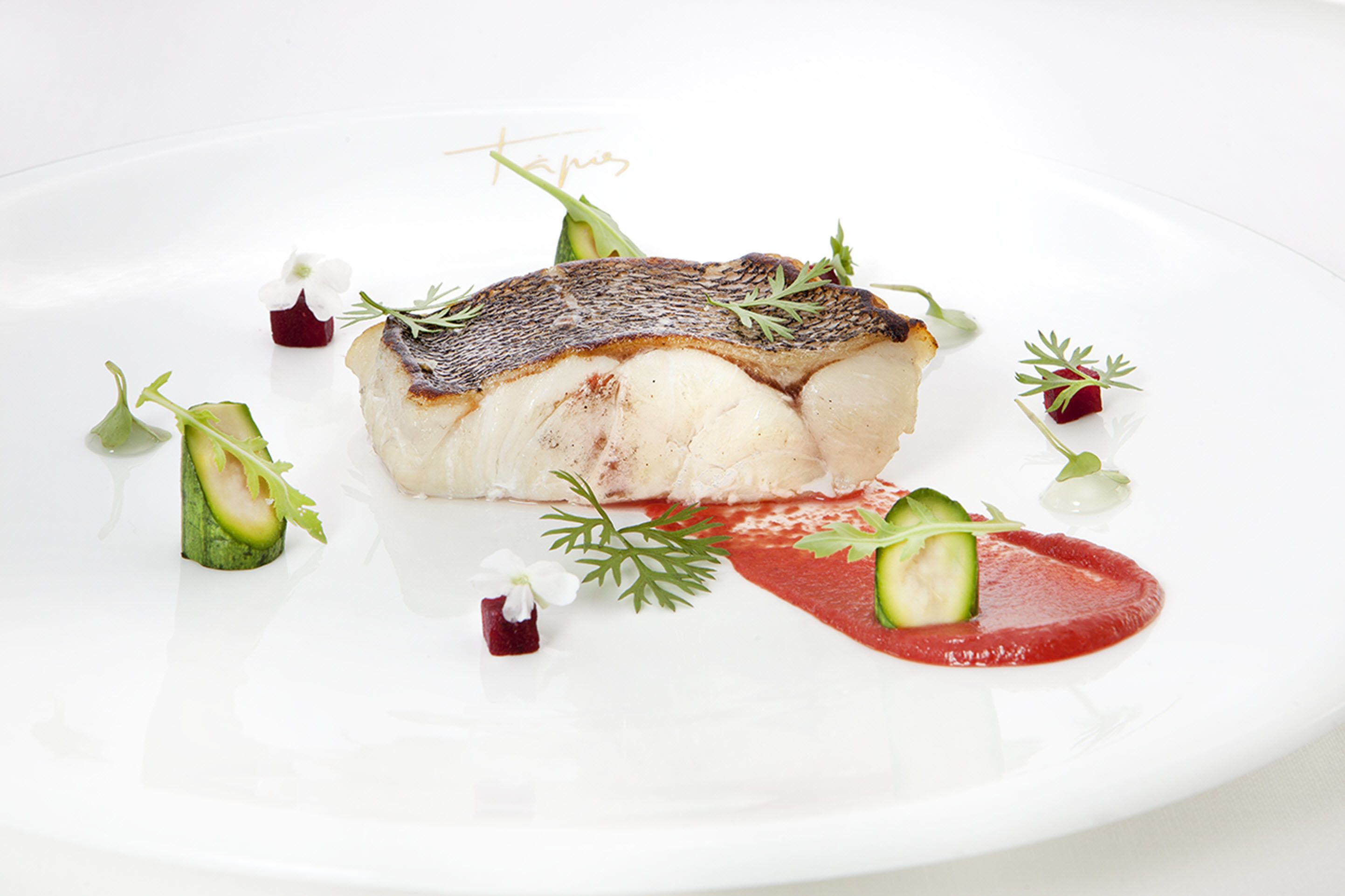Un plato blanco con un trozo de pescado, adornado con hierbas y verduras.