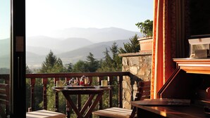 A wooden table with chairs on a balcony overlooking mountains.
