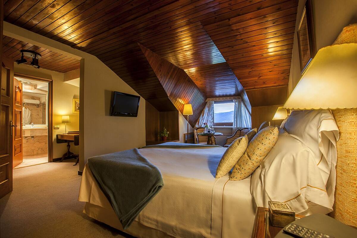 A bedroom with a wooden ceiling, a bed with pillows, a bedside table, and a lamp.