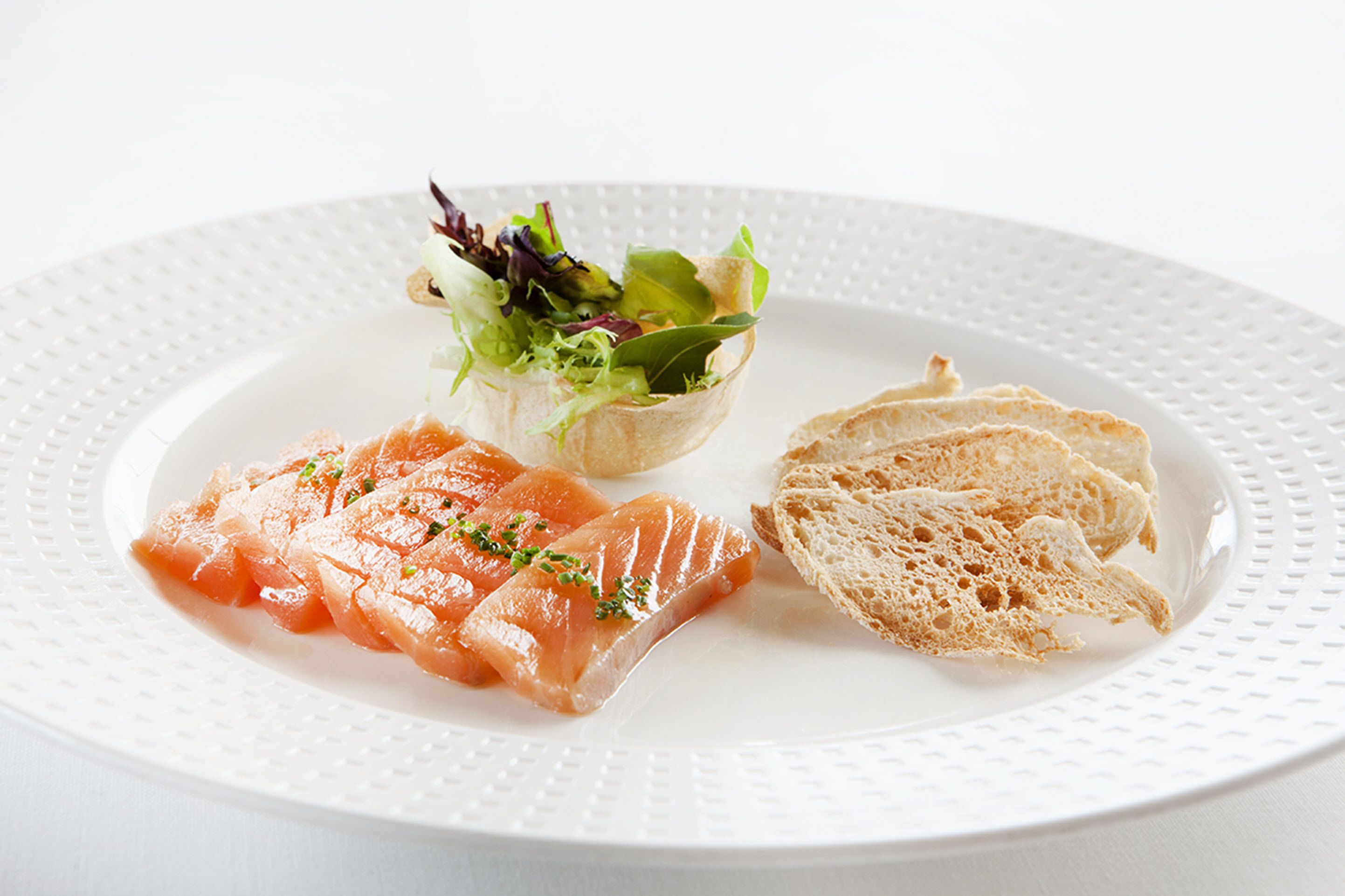 A plate with smoked salmon, a small salad, and slices of bread.