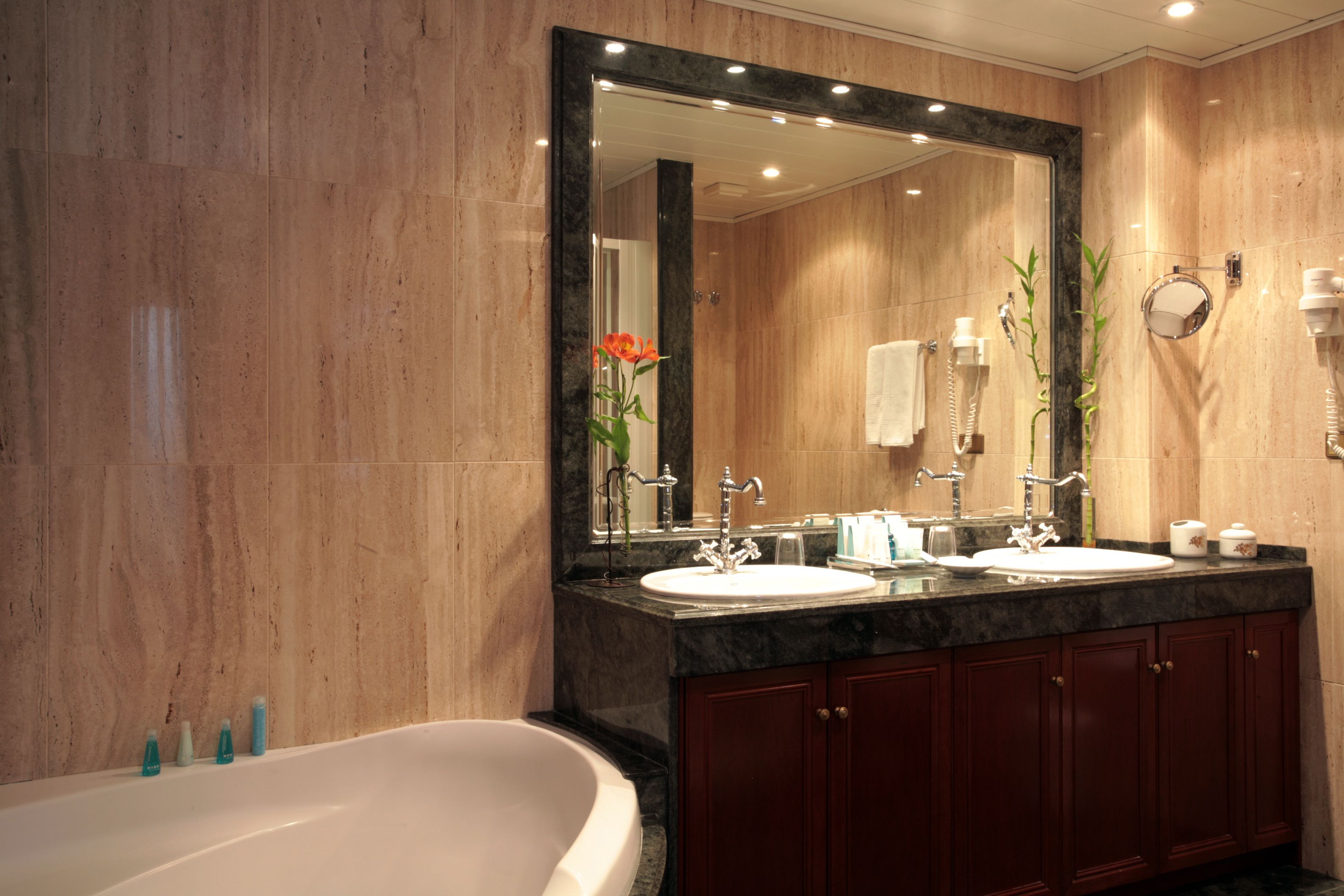 Un baño moderno con un espejo grande, dos lavamanos, una bañera y armarios de madera.