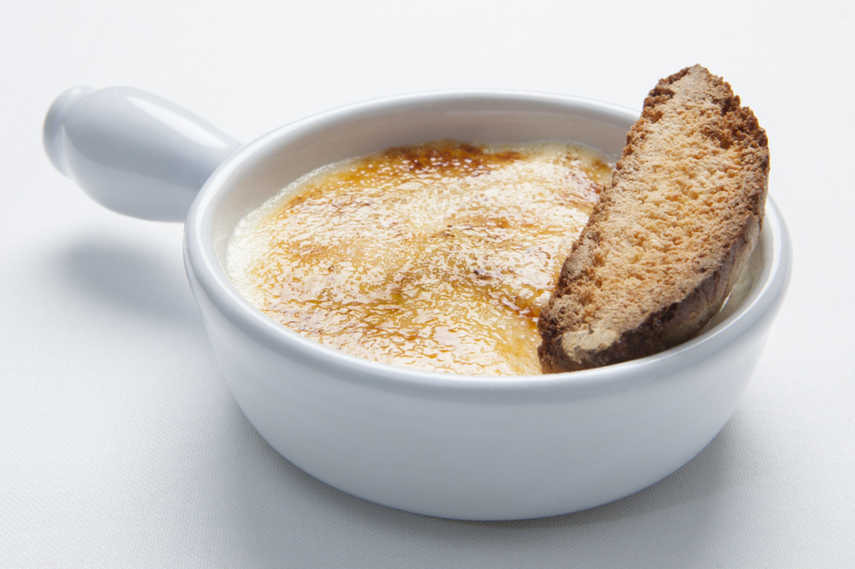 Una taza de cerámica blanca con asa, que contiene una bebida cremosa y una rebanada de pan.