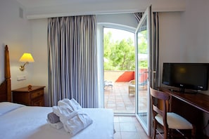 Habitación de hotel con cama, televisión, escritorio y vistas al patio exterior.