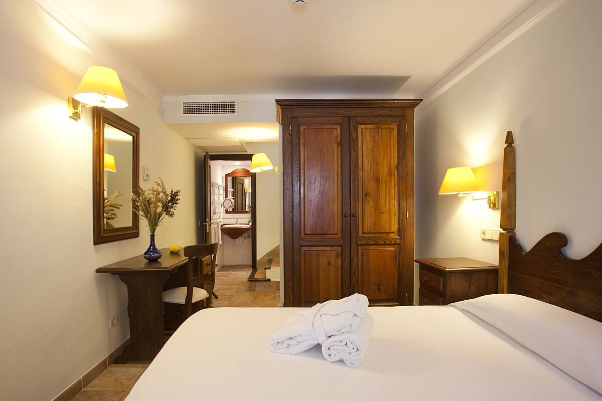 A hotel room with a bed, a desk, a chair, a wardrobe, and a bathroom visible through an open door.