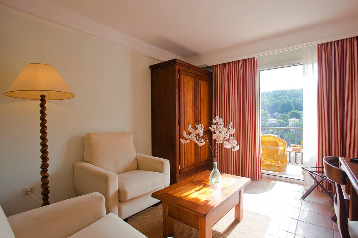 A living room with a sofa, a wooden table with a vase, a lamp, and a view of a balcony with a chair.