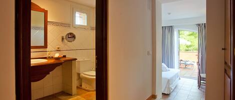 Een hotelbadkamer met een wastafel, toilet en uitzicht op een balkon met een bed en tafel.