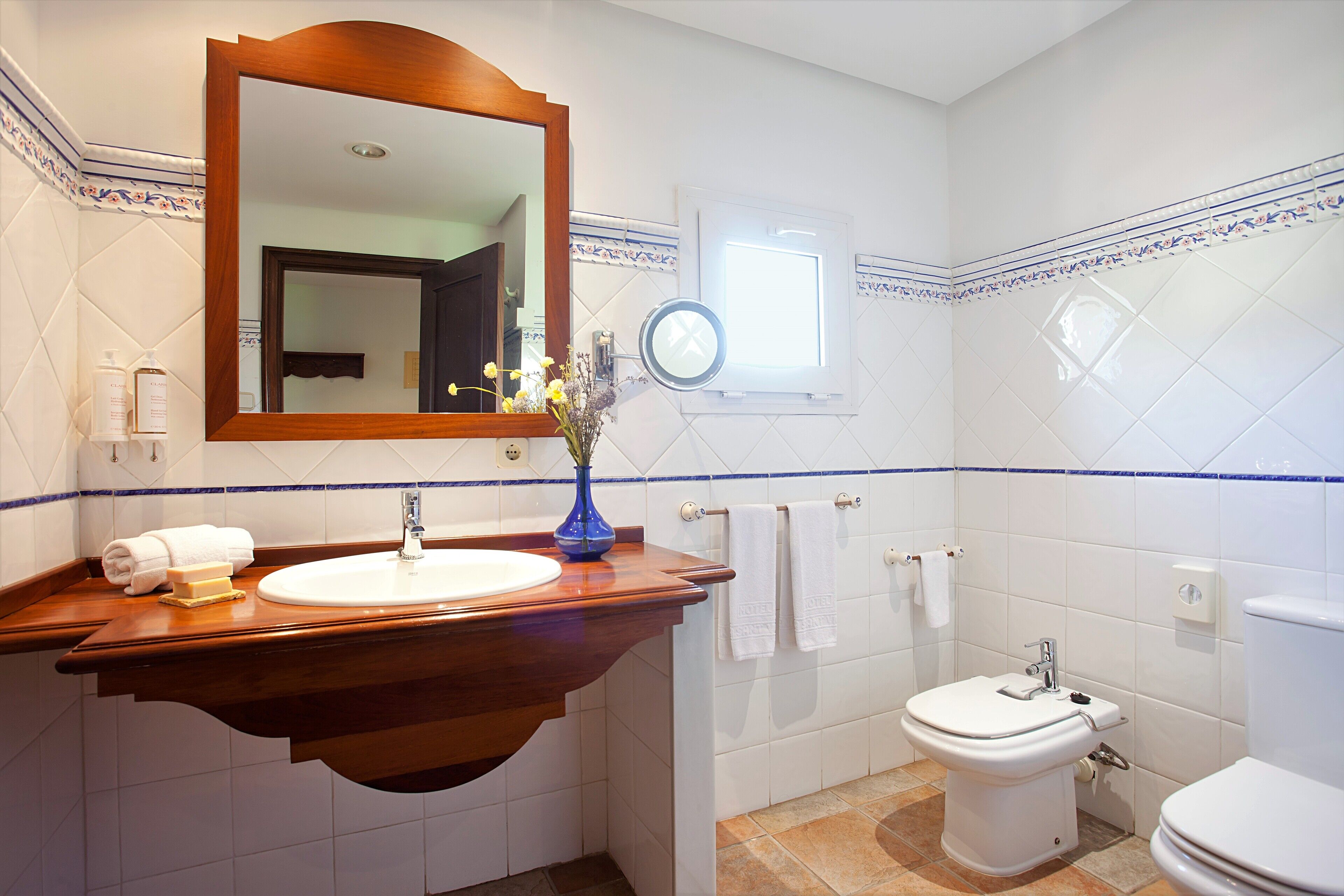 A bathroom with a wooden vanity, a white sink, a mirror, a toilet, and a window.