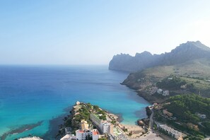 Un pueblo costero con edificios a lo largo del paseo marítimo, una montaña destacada al fondo y aguas azules cristalinas.