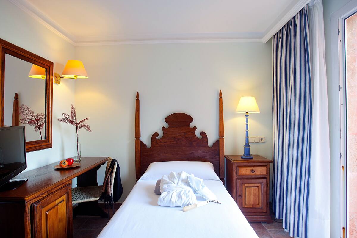 A hotel room with a wooden bed, a desk with a television, a mirror, and two lamps.