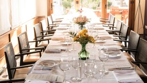 A long dining table set with white tablecloth, chairs, and silverware, with a vase of flowers in the center.