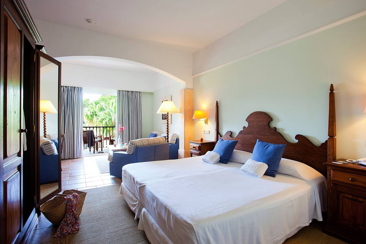 A hotel room with two beds, a sitting area with a chair and a table, and a view of the outdoors.