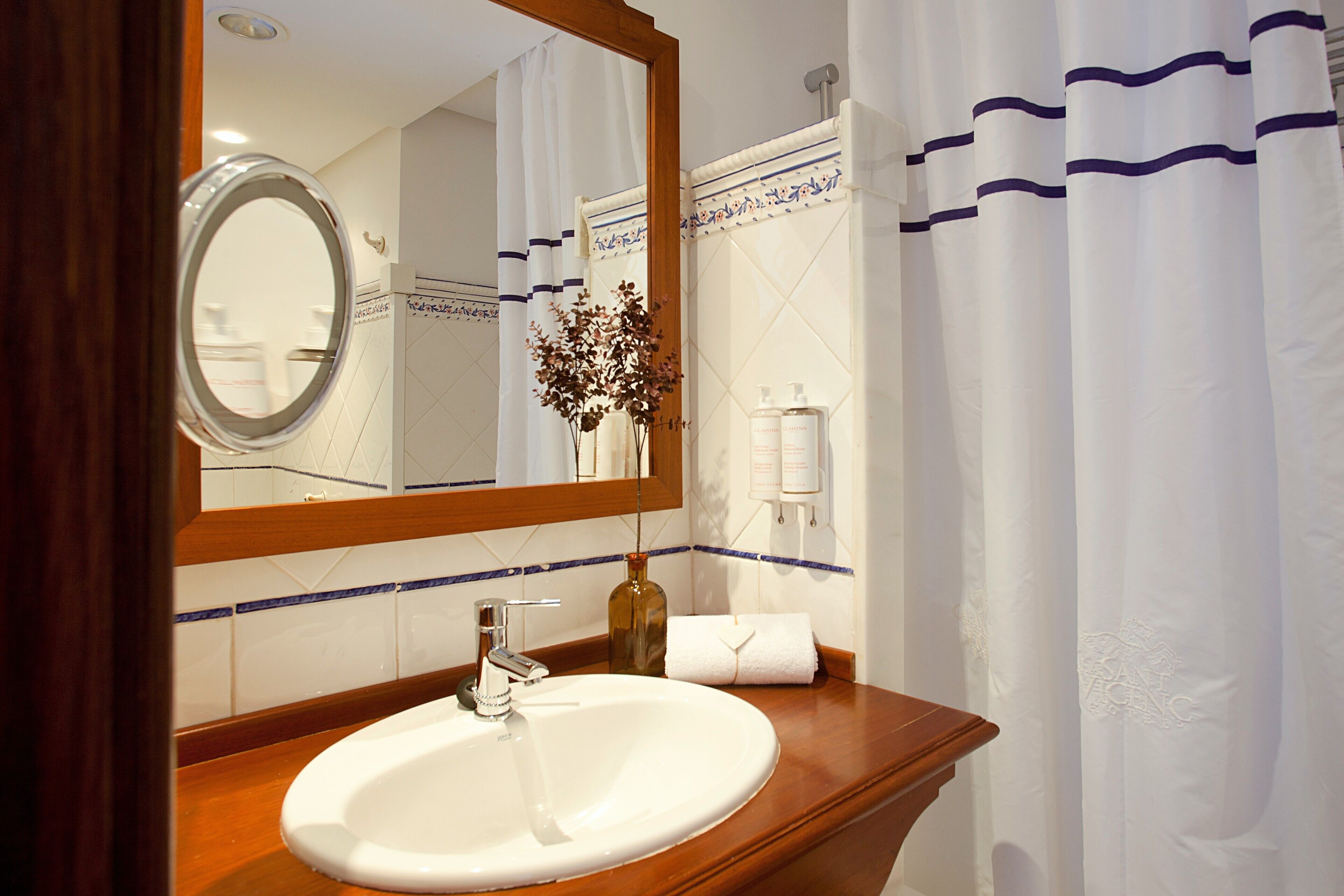 Un baño con tocador de madera, un lavabo blanco, un espejo, una botella de loción y una toalla.