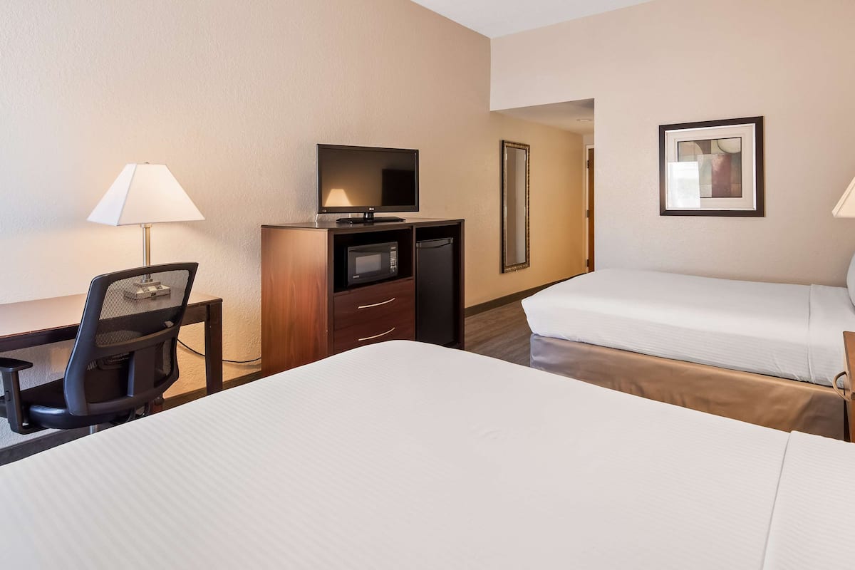 Habitación de hotel con dos camas, un escritorio con una silla, televisor, refrigerador y dos lámparas.