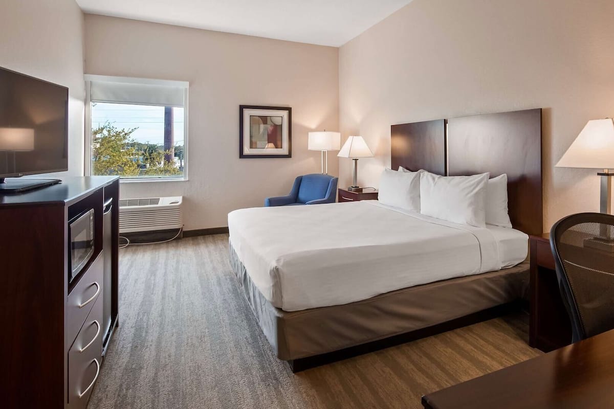 Habitación de hotel con cama, escritorio, silla, televisión y ventana.