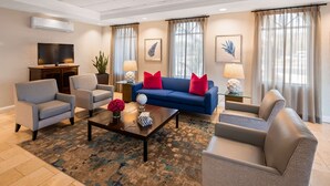 Un salon moderne avec un canapé bleu, deux fauteuils, une table basse agrémentée d’objets décoratifs et un téléviseur.