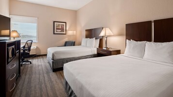 Una habitación de hotel con dos camas, un escritorio con lámpara, una silla y una ventana.