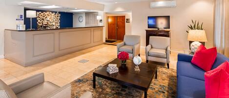 A hotel lobby with a reception desk, seating area, and a television.