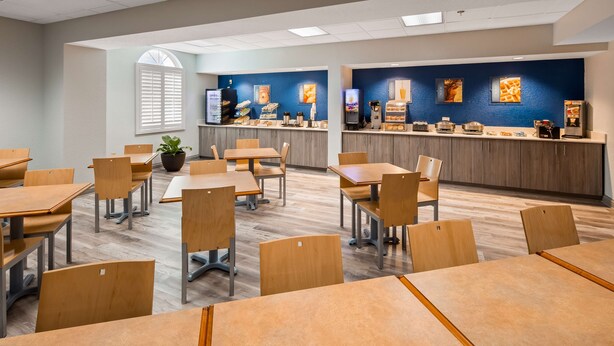 Un espace repas moderne avec des tables et des chaises en bois, un comptoir où sont exposés des plats, et une plante en pot.