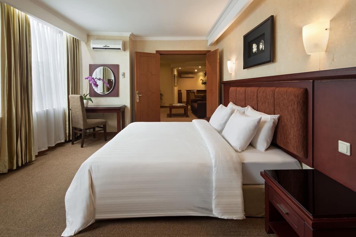 A hotel room with a large bed, a desk with a chair, a mirror, and a television.