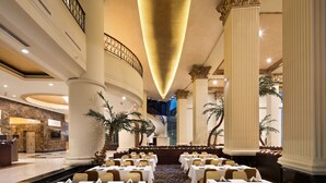 A spacious banquet hall with tiered seating, a central staircase, and a reception area with a marble counter.