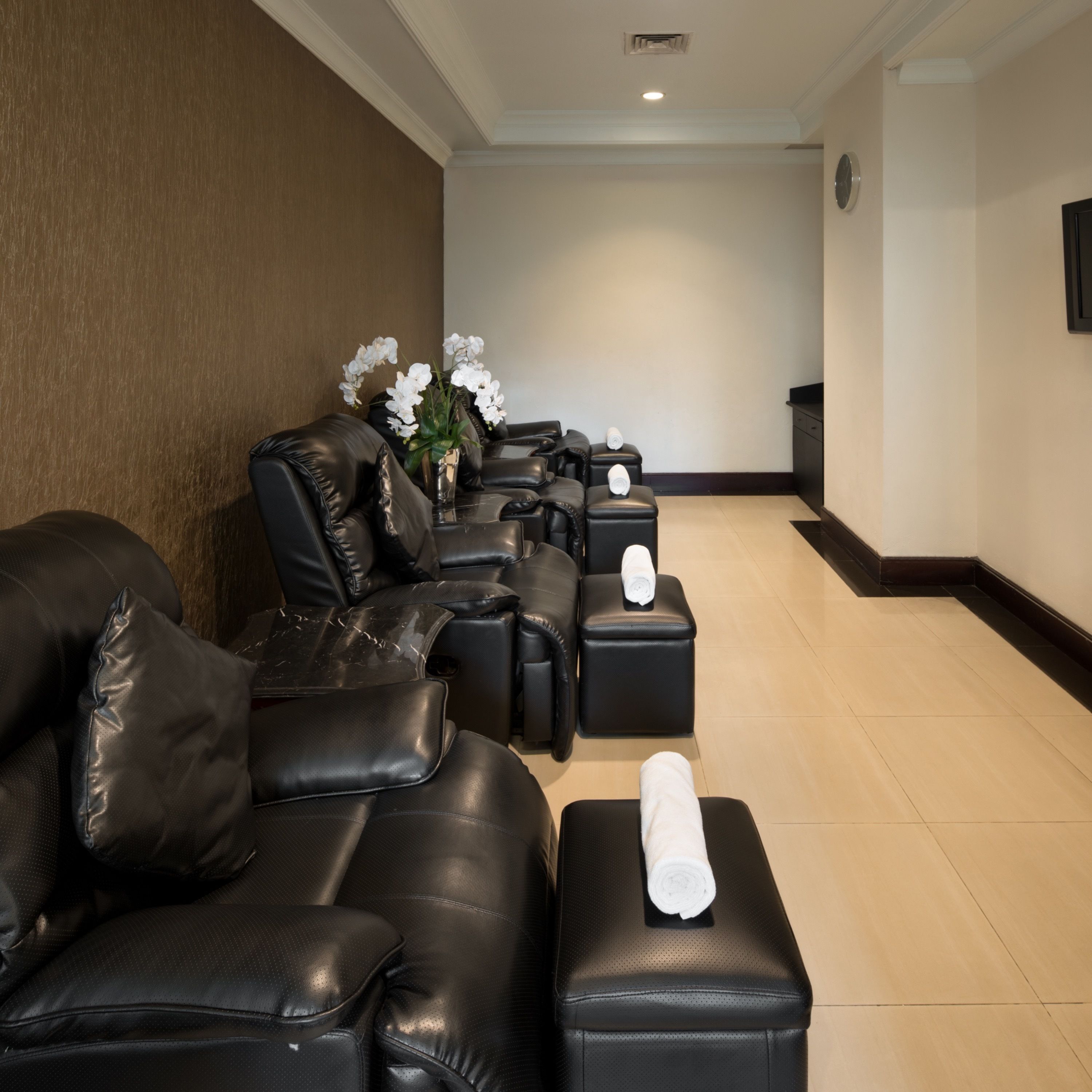 A spa area with black leather chairs and ottomans, a vase with white flowers, and a wall clock.