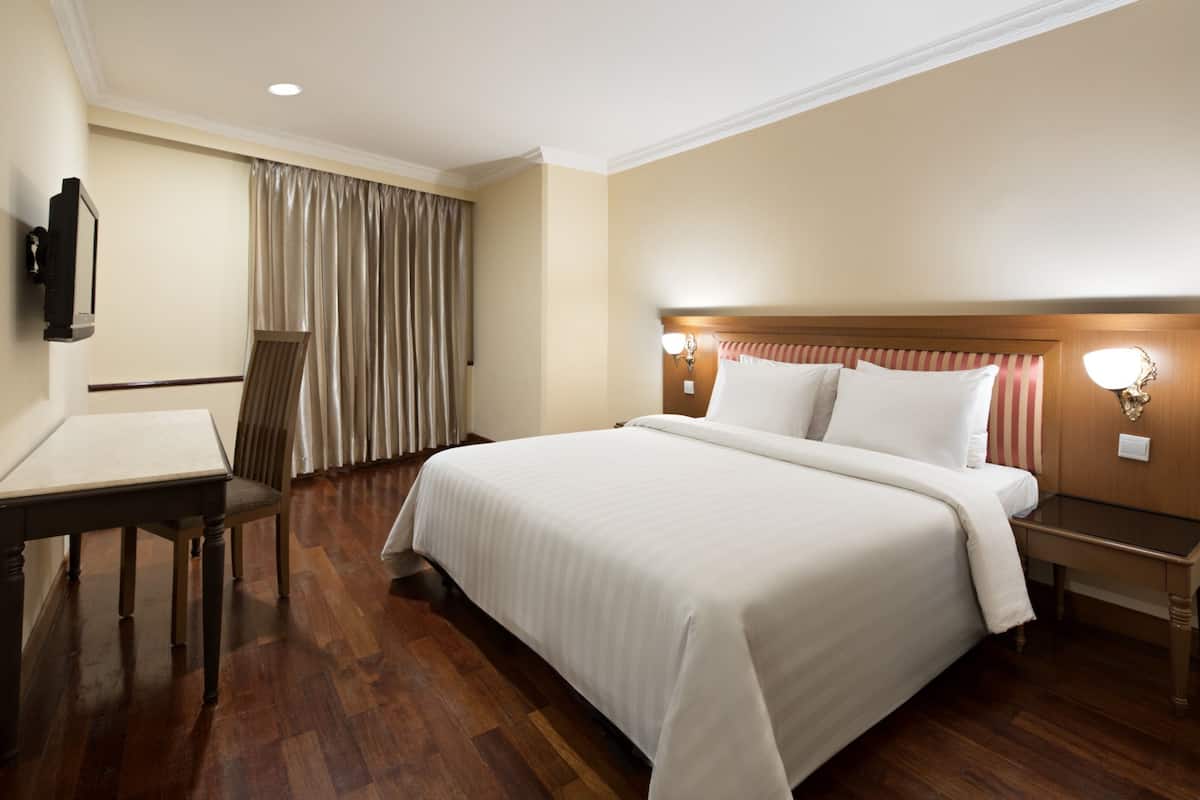 A hotel room with a large bed, a desk, a chair, a television, and a window with curtains.