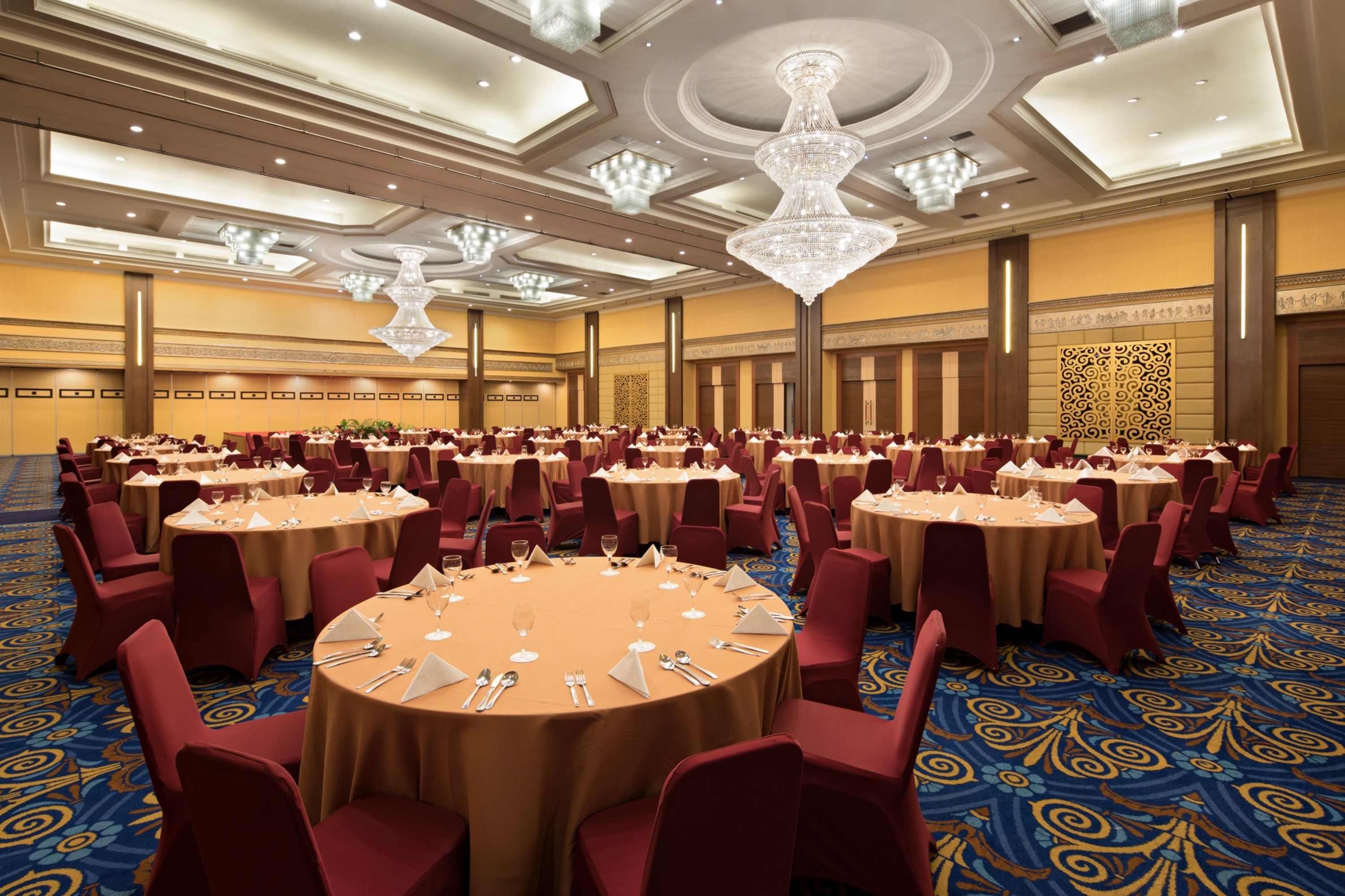 Un salón de banquetes con mesas redondas, sillas rojas y candelabros.