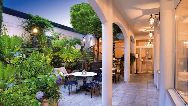 An outdoor patio with a table and chairs, surrounded by lush greenery and potted plants. - Hotel Gloria et Avenue (Lourdes)