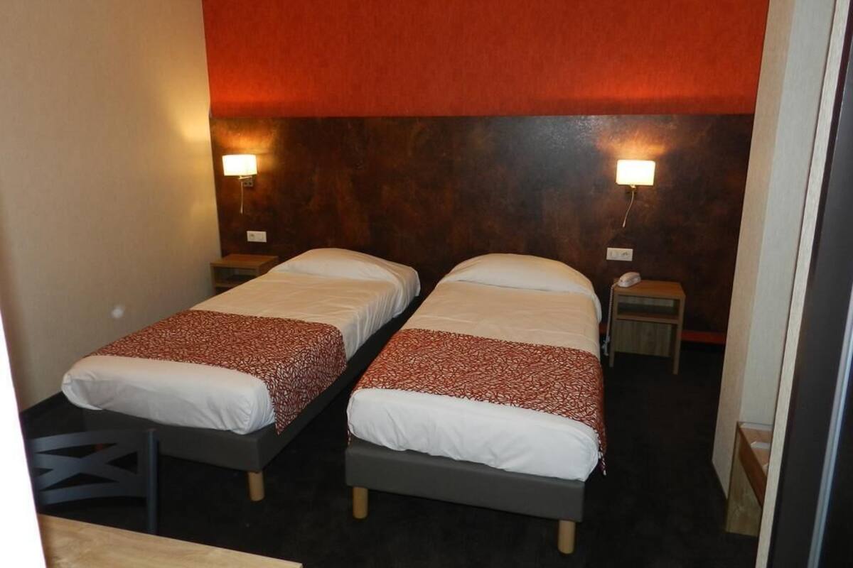 Een hotelkamer met twee eenpersoonsbedden, elk met een nachtkastje en lamp. De kamer heeft een rode accentmuur en een donker hoofdbord.
