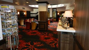A hotel lobby with a reception desk, seating area, and a display of postcards. - Hotel Gloria et Avenue (Lourdes)