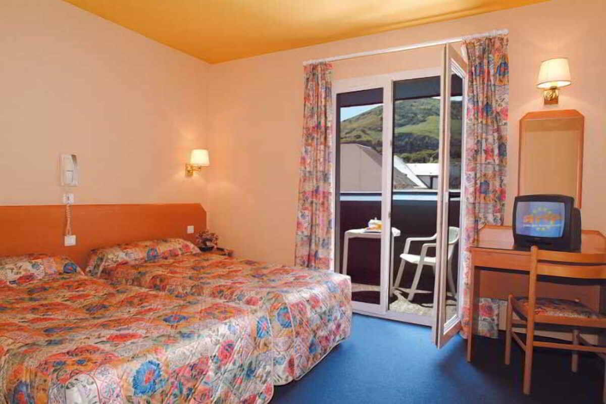 A hotel room with a bed, a desk with a television, and a sliding door to a balcony.