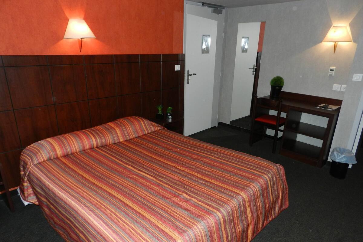 Een hotelkamer met een bed, een bureau, een stoel en een prullenbak.