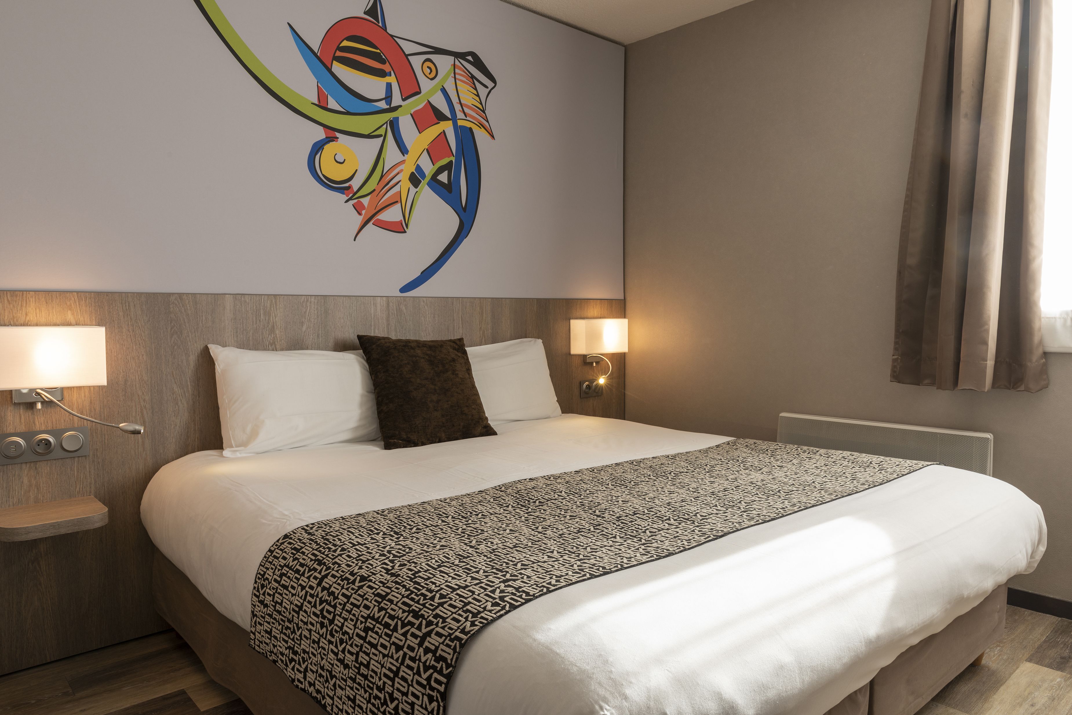 Una habitación de hotel con una cama grande, dos lámparas de noche, una obra de arte en la pared y un ventanal con cortinas.