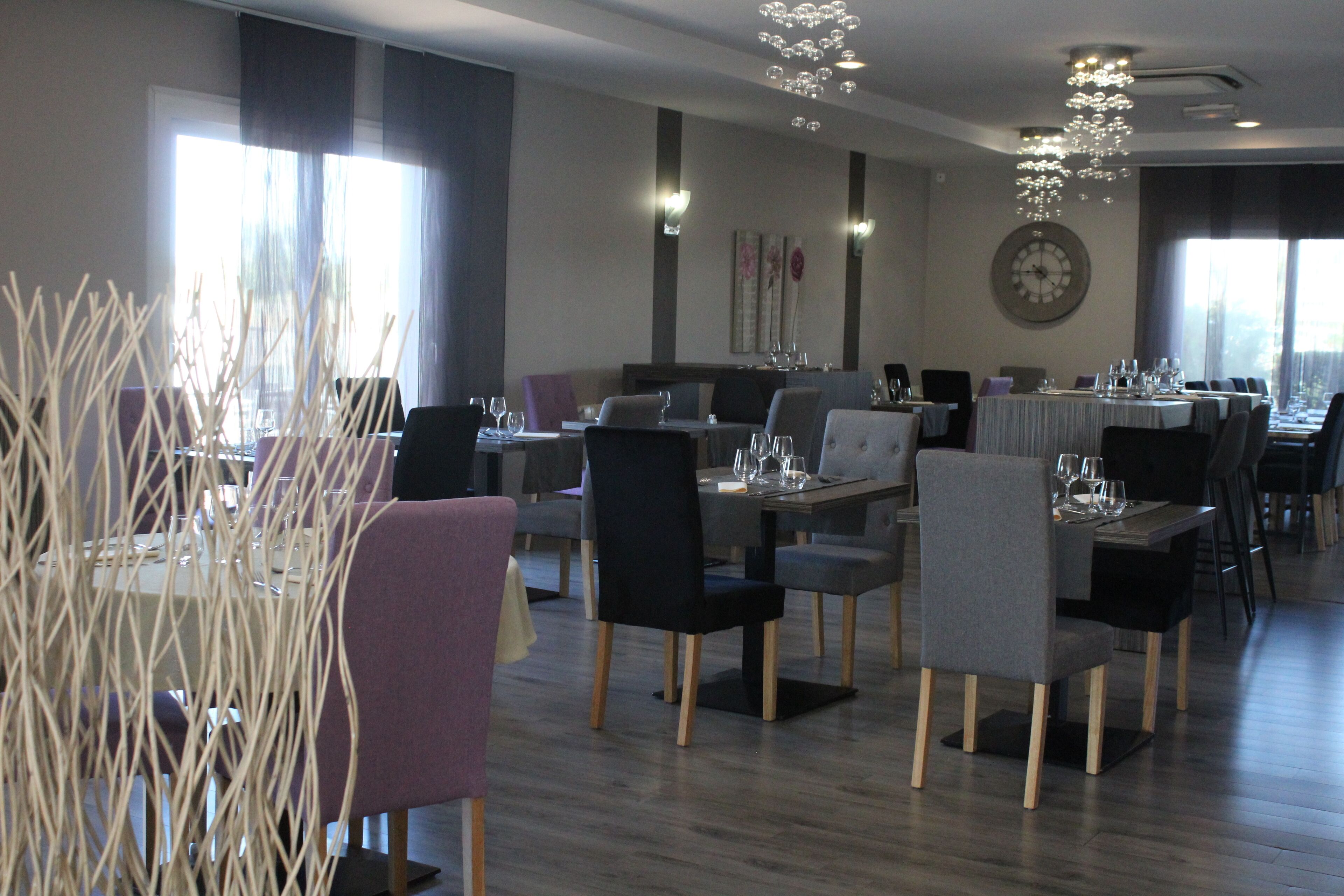 A modern dining area with multiple tables and chairs, a large wall clock, and a decorative light fixture.