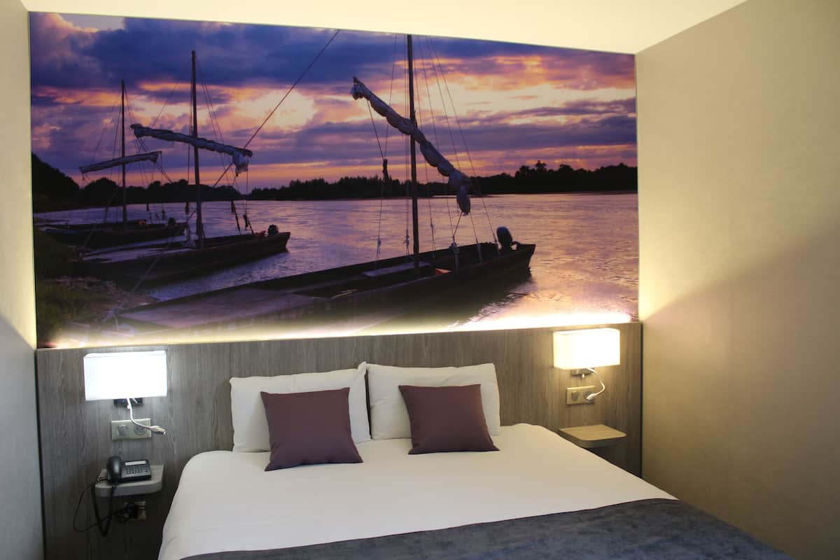 Quarto de hotel com cama, duas mesinhas de cabeceira, um criado-mudo e uma luminária na parede.