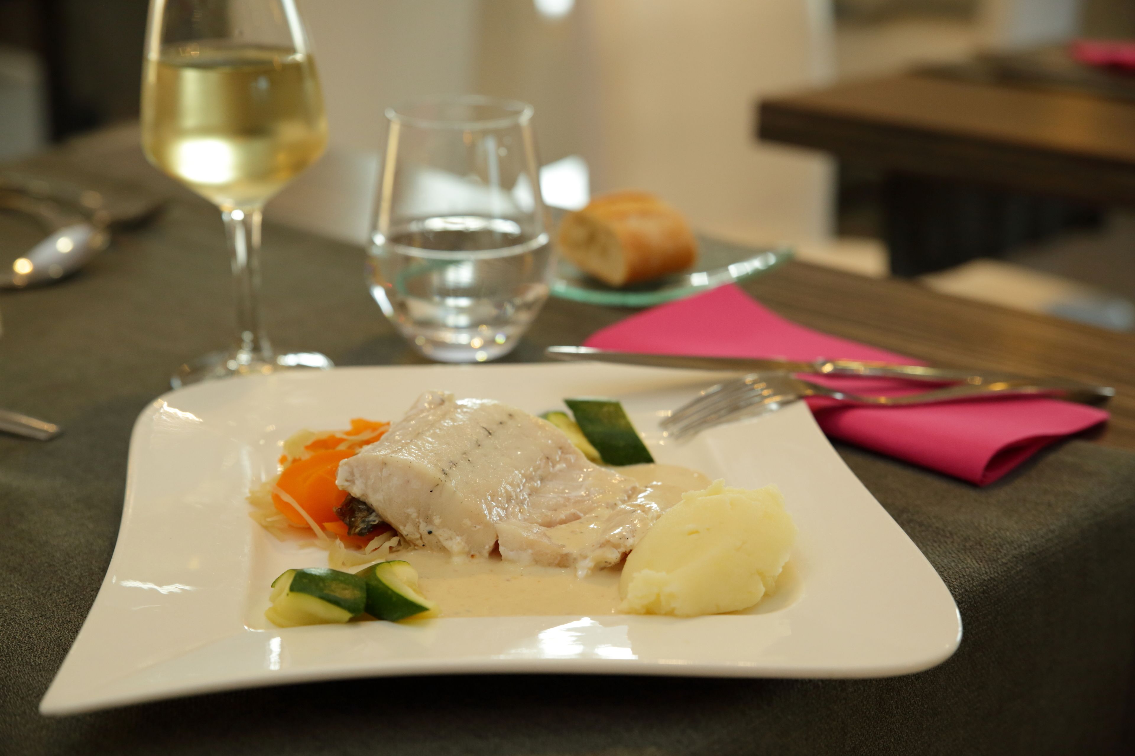 A plate of food with a fish, vegetables, and mashed potatoes, accompanied by a glass of water and a glass of white wine.