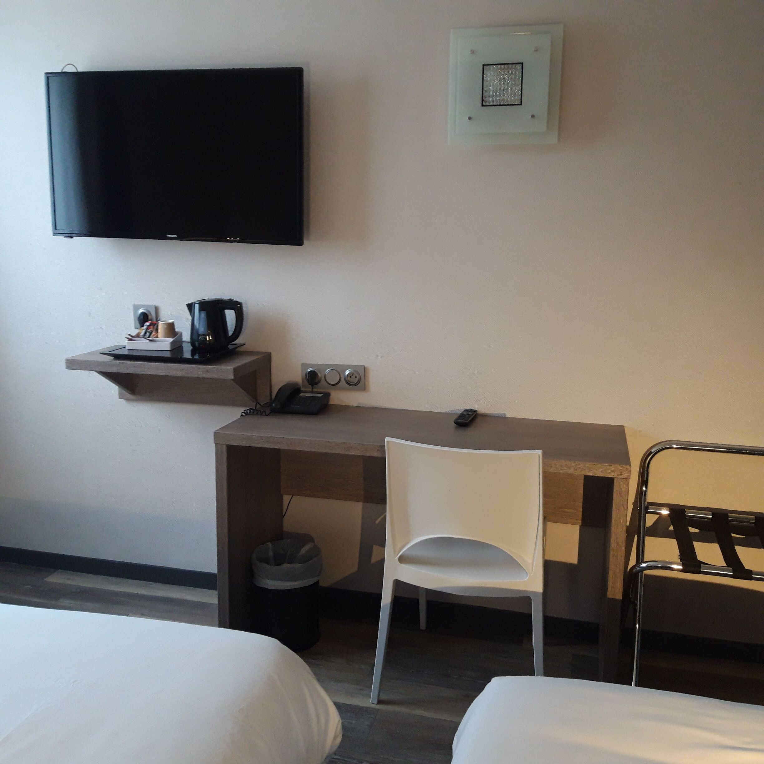 A hotel room with a bed, a desk with a chair, a television, and a small shelf with a coffee maker and other items.
