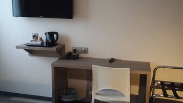 A hotel room with a bed, a desk with a chair, a television, and a small shelf with a coffee maker and other items.