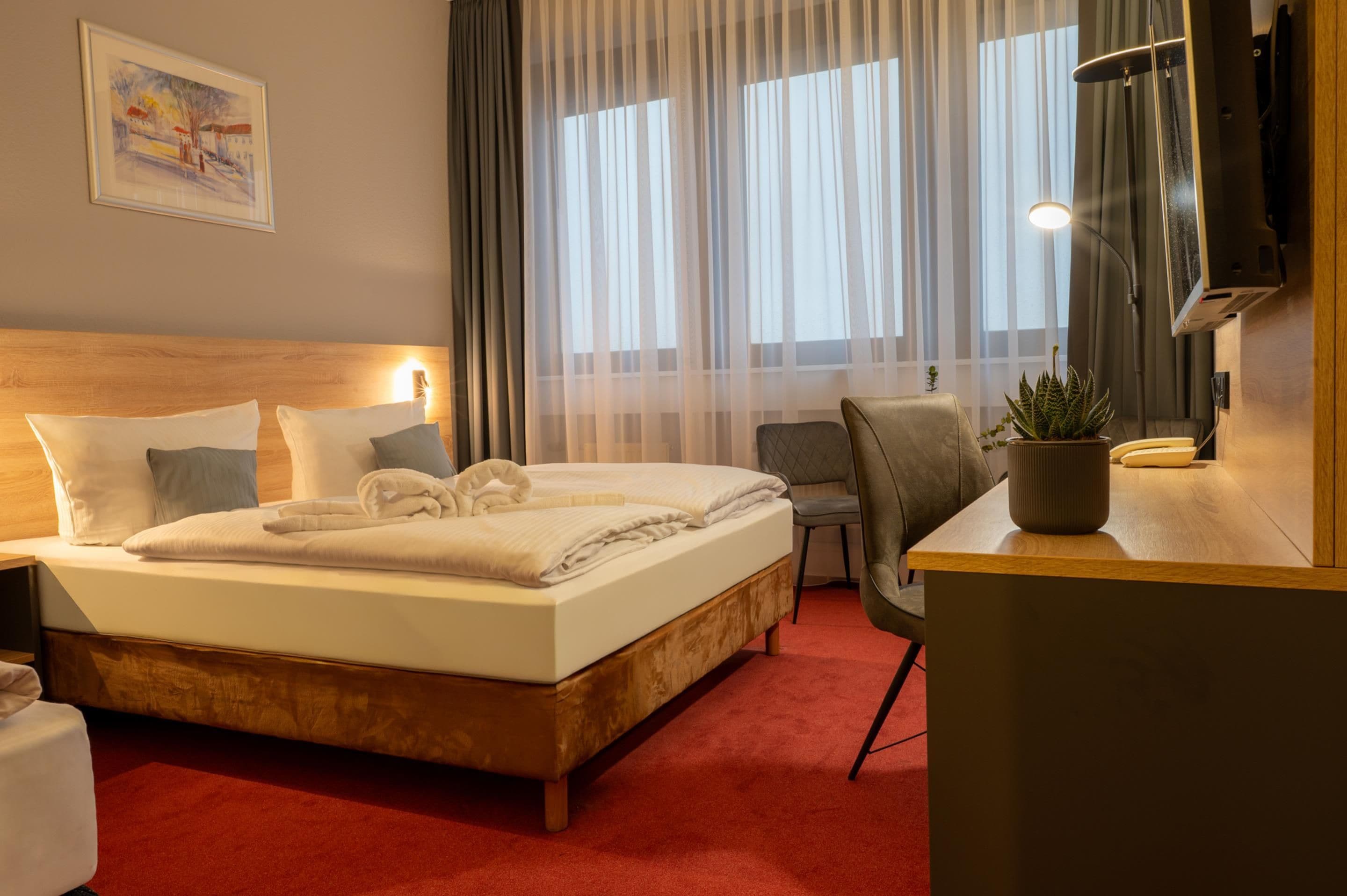 Ein Hotelzimmer mit Bett, Schreibtisch, Stuhl, Fernseher und Pflanze.