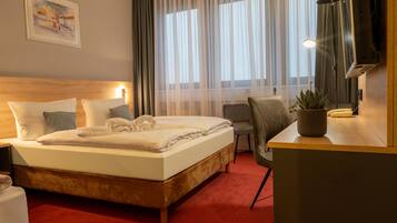 Ein Hotelzimmer mit Bett, Schreibtisch, Stuhl, Fernseher und Pflanze.