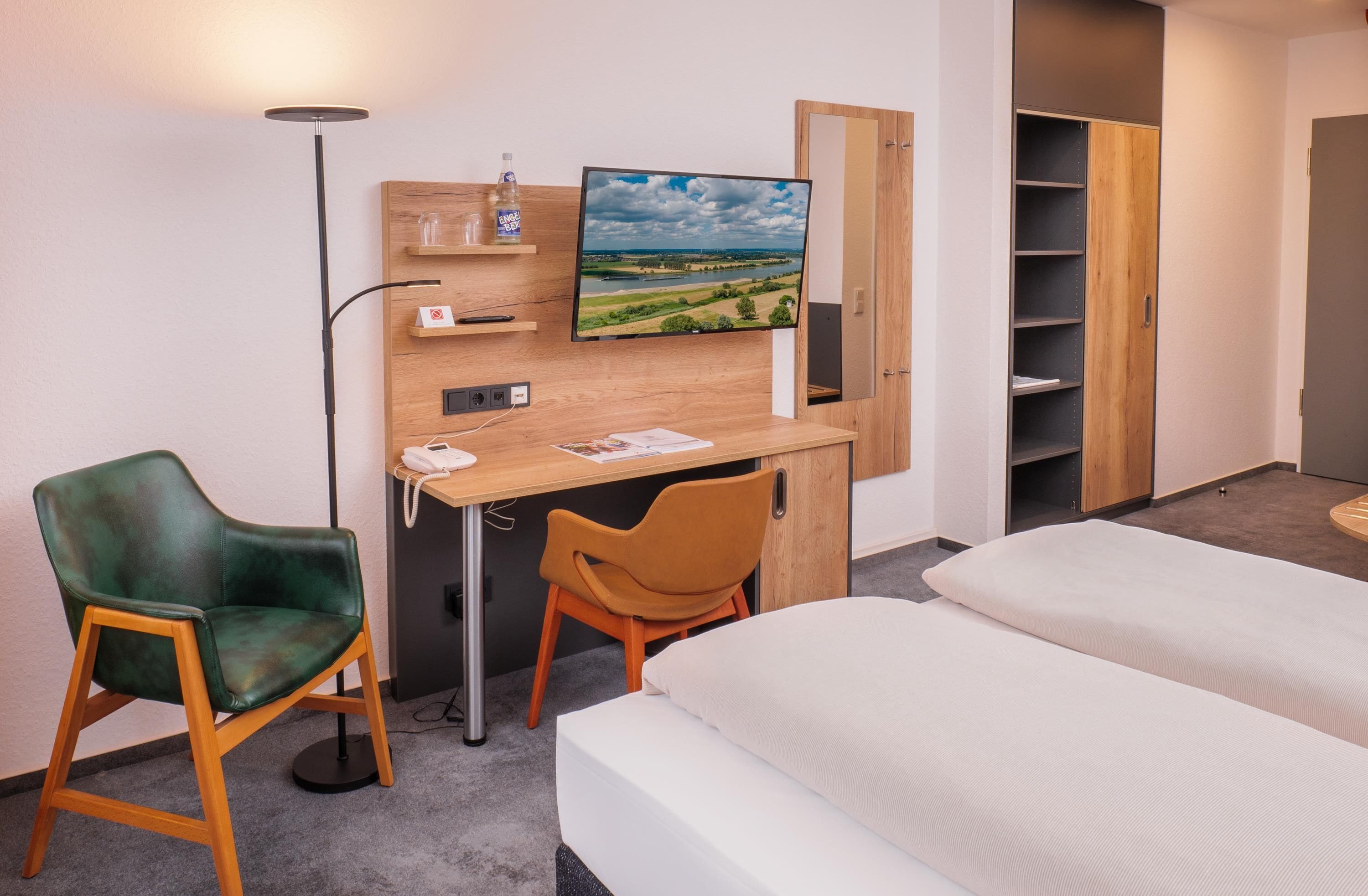 Una habitación de hotel con escritorio, dos sillas, una cama, televisor y armario.