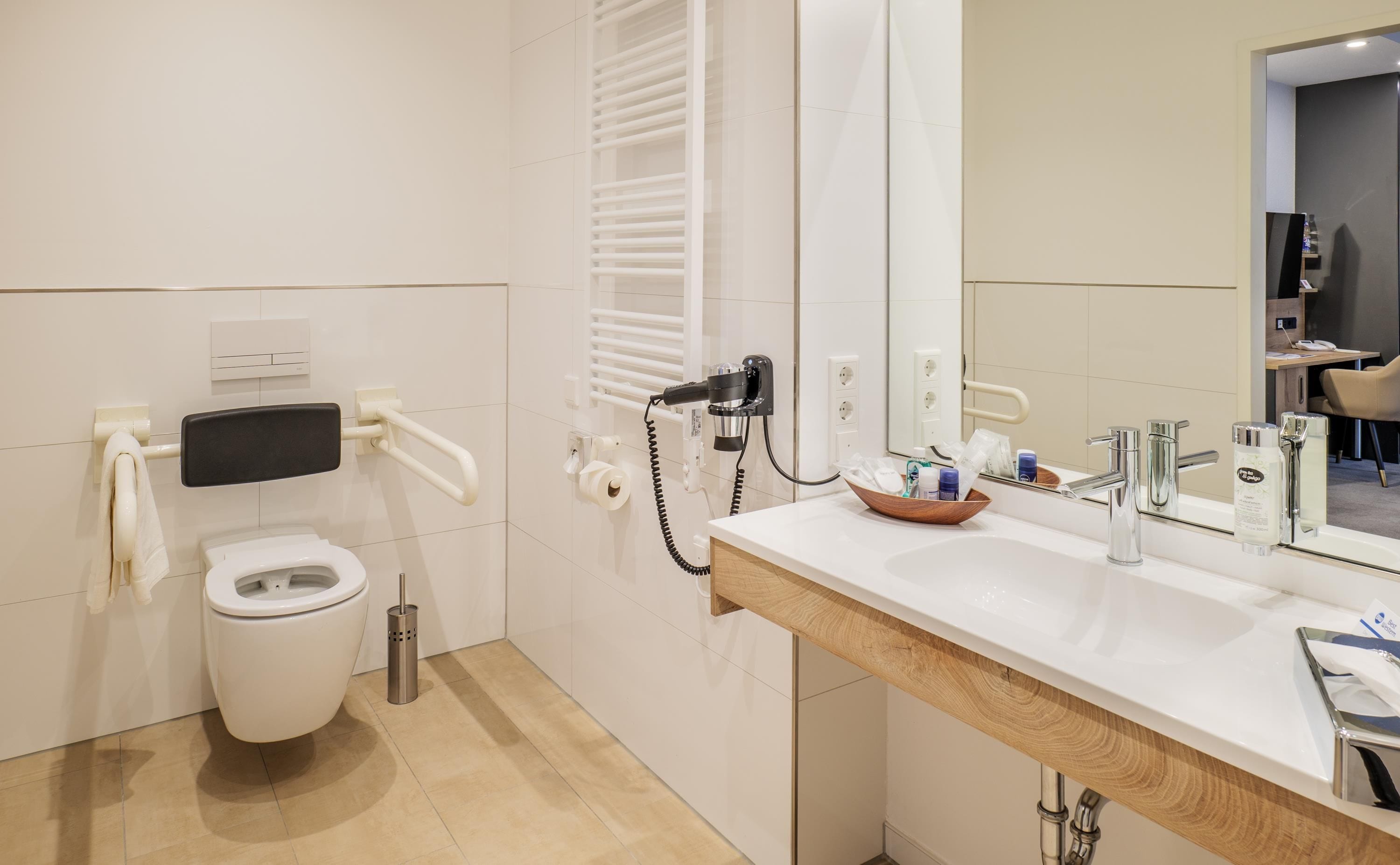 Ein modernes Badezimmer mit Toilette, Handtrockner, Handtuchhalter und einem Waschtisch mit Spiegel.