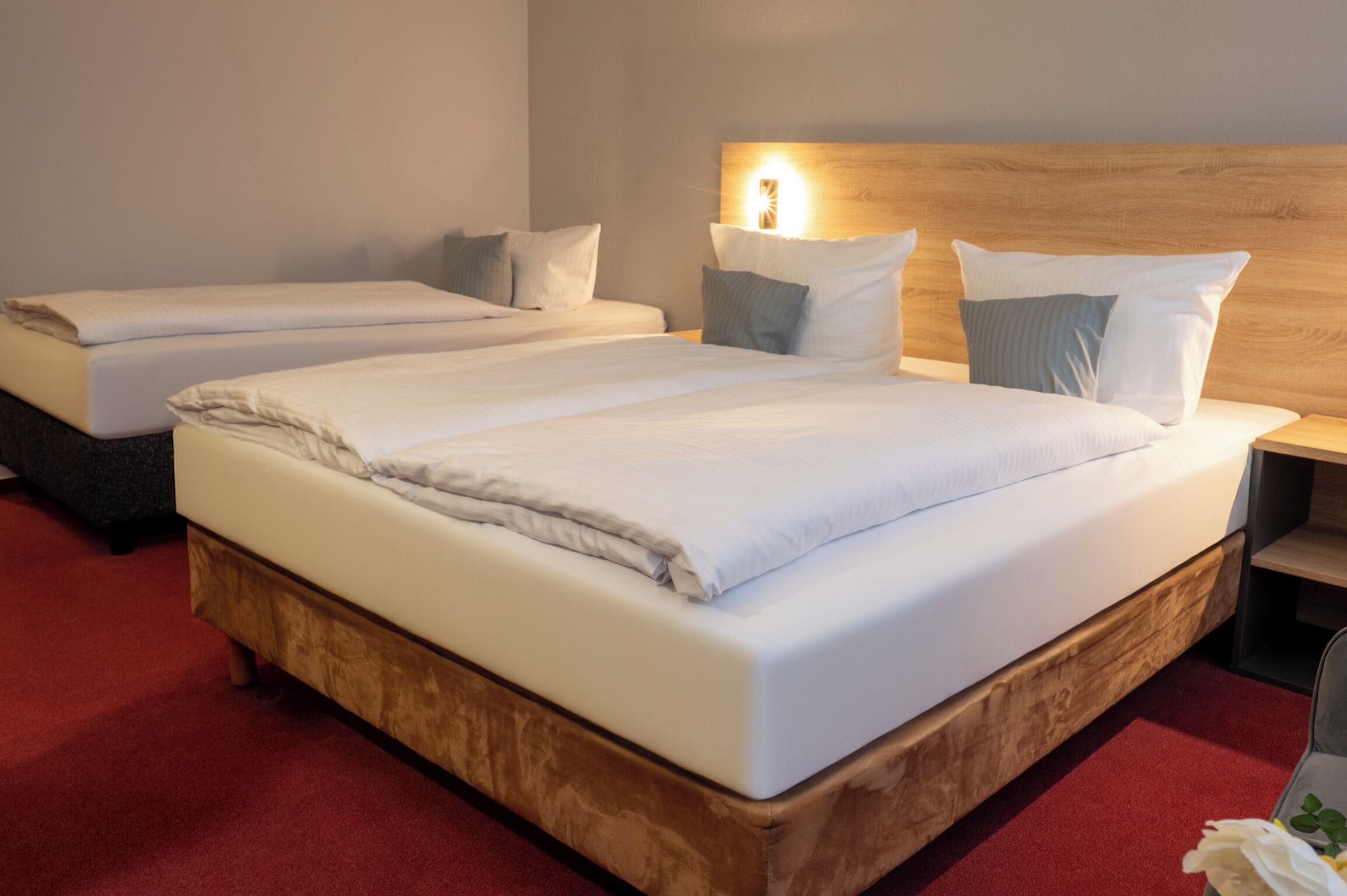 A hotel room with two single beds, wooden headboards, and a red carpet.
