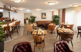 A hotel dining area with multiple tables and chairs, a bar area, and a seating area with a sofa.
