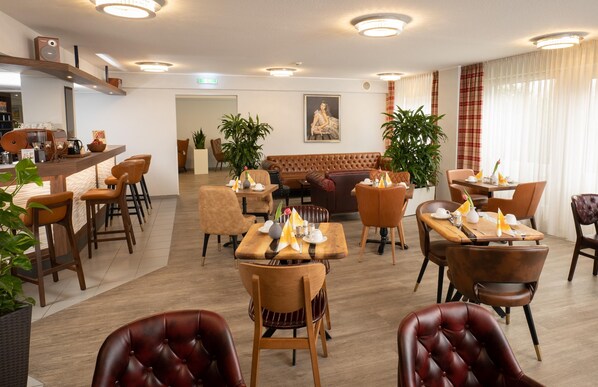Un comedor de hotel con varias mesas y sillas, una zona de bar y un área de descanso con un sofá.