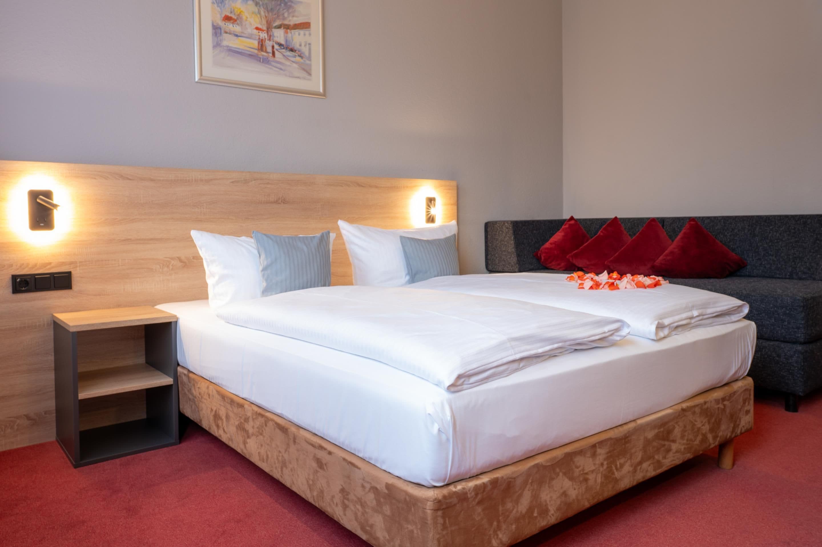 A neatly made bed with white linens, a wooden headboard, and two bedside tables with wall-mounted lamps.