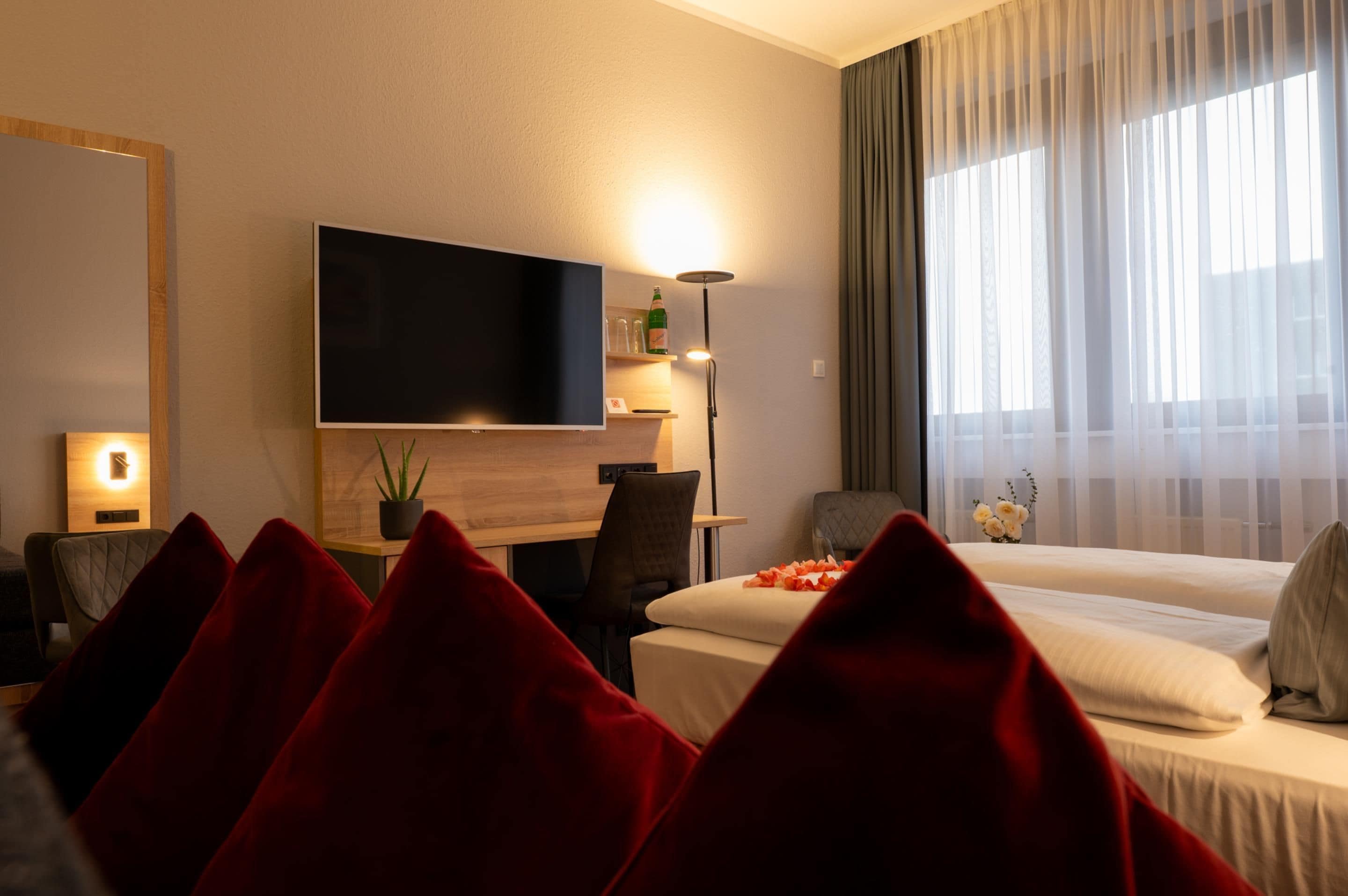 Habitación de hotel con cama, escritorio, silla, televisor y ventana con cortinas.