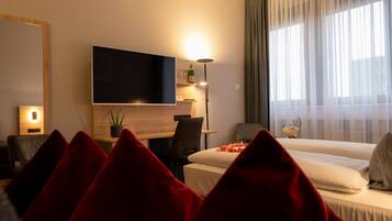 Habitación de hotel con cama, escritorio, silla, televisor y ventana con cortinas.