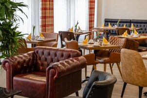 L’intérieur d’un restaurant avec des sièges en cuir, des tables dressées avec de l’assiette blanche et des rideaux à carreaux rouges.