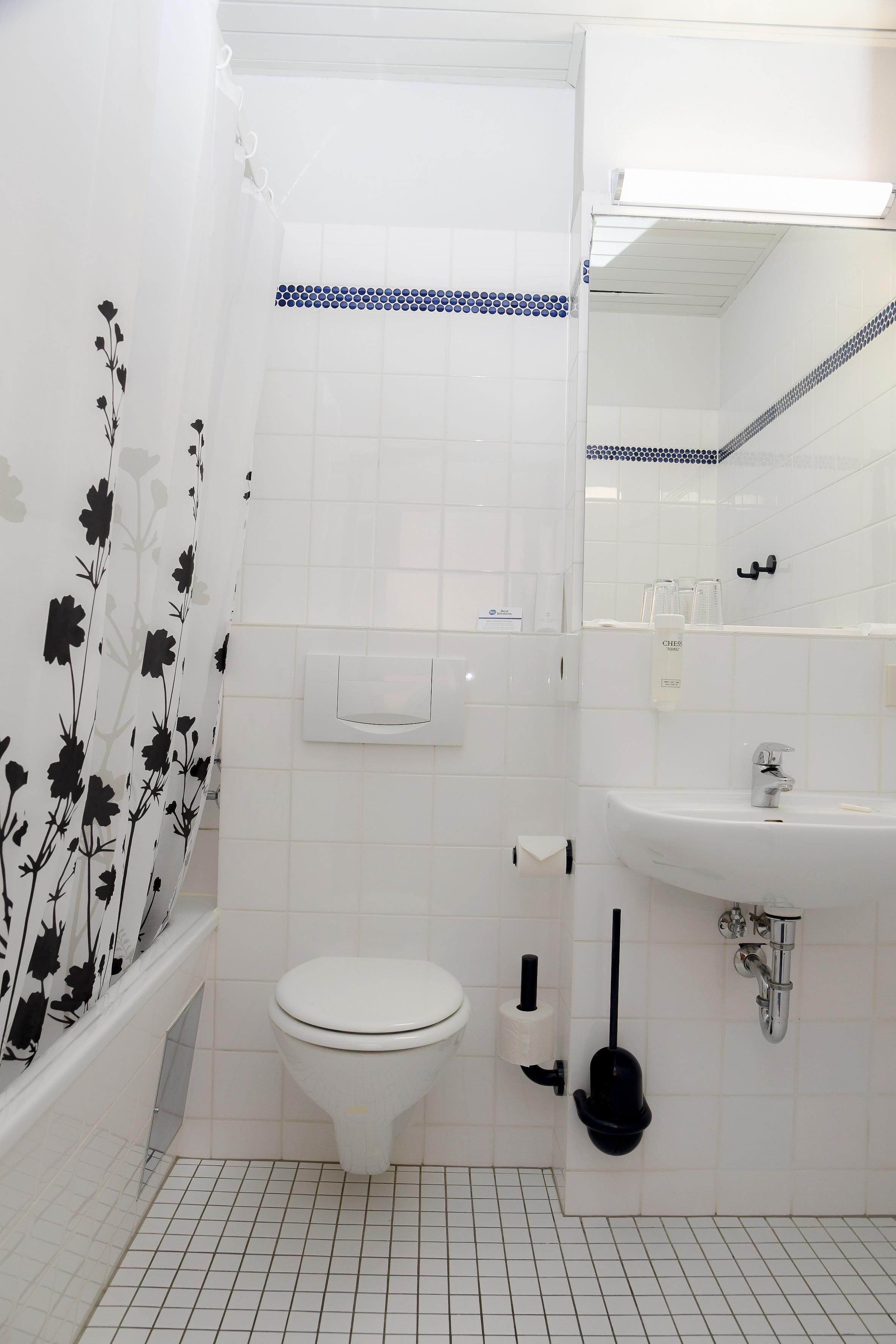 A bathroom with a toilet, a sink, a shower, and a toilet paper holder.